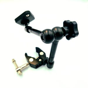 Könnte beinhalten: Ein schwarzer Gelenkarm mit Klemme und Kugelkopf. Der Arm hat eine quadratische Montageplatte und einen sternförmigen Knopf zur Einstellung. Die Klemme hat eine silberfarbene Schraube. Das Produkt ist für die Montage von Zubehör konzipiert.