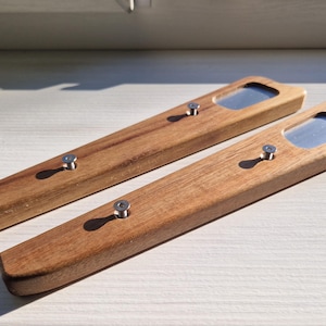 Puede incluir: Dos abridores de botellas de madera con inserciones metálicas. Los abridores son de madera marrón claro y tienen forma rectangular. Cada abridor tiene un pequeño tornillo de metal en el centro.