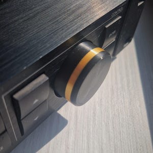 May include: Close-up of a black knob with a gold accent ring. The knob is part of a black electronic device with buttons labelled "Control" and "Enter".