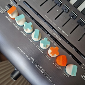 Könnte beinhalten: Nahaufnahme eines Musik-Mixers mit Knöpfen und Schiebereglern. Die Knöpfe sind mit Texten wie "FX Send 1", "High EQ", "Mid Freq", "Low EQ", "EQ Trim", "Resonance", "Pan" und "Cutoff" beschriftet.