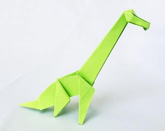 Puede incluir: Un dinosaurio de origami verde con un cuello largo y una cabeza pequeña. El dinosaurio está de pie sobre una superficie blanca.