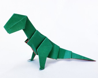 Puede incluir: Un dinosaurio de origami verde, doblado de papel, con una cola larga y una cabeza pequeña. El dinosaurio está de pie sobre una superficie blanca.