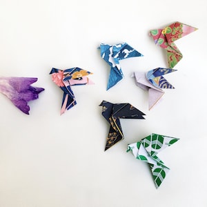 May include: A collection of six origami birds made from patterned paper. The birds are in various colours, including blue, green, red, and purple. They are arranged on a white background.