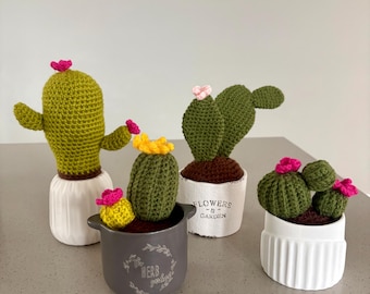 Puede incluir: Cuatro cactus de ganchillo en varias macetas. Un cactus verde alto en una maceta blanca acanalada, un cactus pequeño amarillo y verde en una maceta gris con la etiqueta "HERB garden", un cactus verde plano en una maceta blanca con la etiqueta "FLOWERS & GARDEN" y un cactus verde redondo en una maceta blanca acanalada.