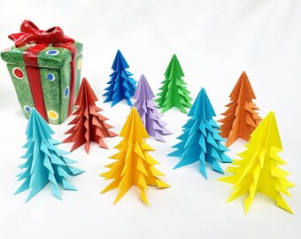 Puede incluir: Una colección de diez árboles de papel plegado en varios colores, incluyendo azul, rojo, amarillo, verde, naranja y morado, dispuestos cerca de una caja de regalo de cerámica verde con tapa roja y lunares de colores.