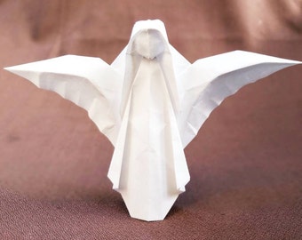 Puede incluir: Un ángel de origami blanco con las alas extendidas. El ángel está doblado de una sola hoja de papel y tiene un diseño simple y elegante.