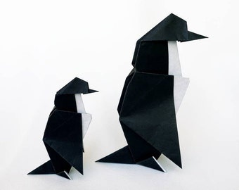 Puede incluir: Dos pingüinos de origami hechos de papel negro con detalles blancos. El pingüino más grande está de pie, mientras que el pingüino más pequeño está de pie a la izquierda del más grande.