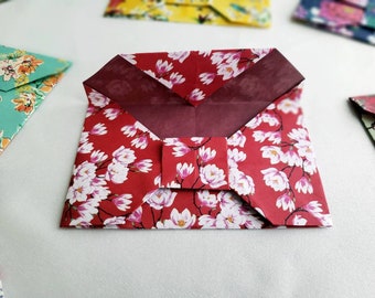 Puede incluir: Un sobre de origami rojo con un patrón floral blanco. El sobre está doblado en un estilo japonés tradicional con una solapa en la parte delantera.