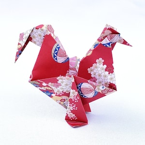 May include: A red origami crane with a floral pattern. The crane is folded from paper with a red background and white and pink flowers.