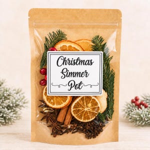 May include: A clear pouch with a kraft paper backing containing dried orange slices, cinnamon sticks, star anise, whole cloves, cranberries, and evergreen sprigs. A white label on the front reads Christmas Simmer Pot in black script text.