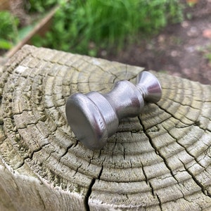 May include: A silver metal hammer with a rounded head and a textured handle. The hammer is resting on a weathered wooden surface.