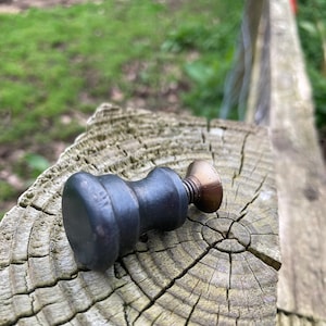 May include: A black and brass knob with a rounded top and a threaded base, resting on a weathered wooden surface.