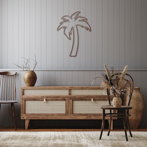 May include: A wooden cabinet with four drawers and a woven rattan front. The cabinet is brown and has brass handles. A wooden chair with a woven rattan seat and back is in front of the cabinet. A vase with dried branches is on the left side of the cabinet. A vase with dried flowers is on the right side of the cabinet. A wooden palm tree cutout is on the wall behind the cabinet.
