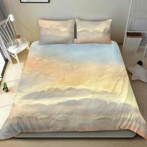 Pode incluir: Um conjunto de roupa de cama macio, azul claro, amarelo e branco com um padrão de nuvens em estilo aquarela. O conjunto de roupa de cama inclui uma capa de edredom e duas fronhas.