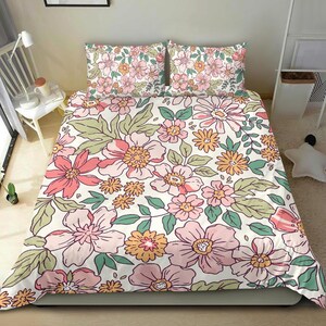 May include: A floral bedding set featuring a duvet cover and two pillowcases. The design showcases large, stylized flowers in shades of pink, peach, yellow, and green against a white background. The bedding set is designed to fit a bed.