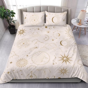May include: A white bedding set with a gold celestial pattern. The pattern includes stars, moons, suns, and clouds. The bedding set includes a duvet cover and two pillowcases.
