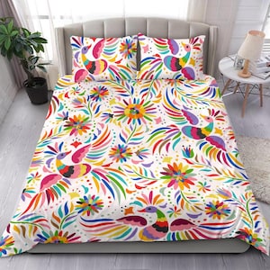 Può includere: Un set di biancheria da letto bianco con un vivace motivo multicolore di uccelli e fiori stilizzati. Il design include motivi ripetuti di uccelli con lunghe piume di coda curve e varie forme floreali nelle tonalità del rosa, blu, giallo, verde e viola, che coprono sia il copripiumino che due federe abbinate.