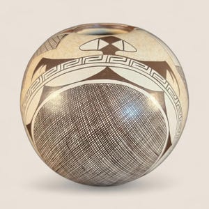 Puede incluir: Una olla de cerámica redonda de color crema con intrincados diseños geométricos en blanco y negro. La olla presenta un patrón de trama cruzada en la mitad inferior y una serie de formas y líneas estilizadas alrededor de la parte superior. Tiene una pequeña abertura en la parte superior.