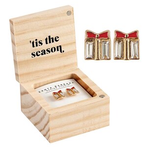 Op de afbeelding: Een houten doos met een scharnierend deksel en een wit label met de tekst 'tis the season'. De doos bevat een paar gouden oorbellen in de vorm van cadeaudoosjes met rode strikken en heldere strass steentjes.