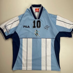 May include: Light blue and white striped soccer jersey with the number 10 on the front. Features the Fila logo, a player graphic, and a signature. The sleeves are white with navy blue trim. The collar is navy blue and white.