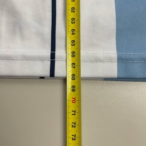 May include: Close-up of a white and light blue fabric with a dark blue stripe. A yellow measuring tape shows measurements from 59 to 75 inches.