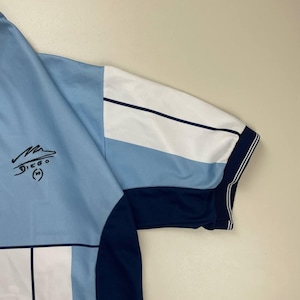 May include: Light blue and white soccer jersey with a navy blue sleeve and trim. The jersey features a signature and the name "DIEGO" with the number "10" printed on the front.