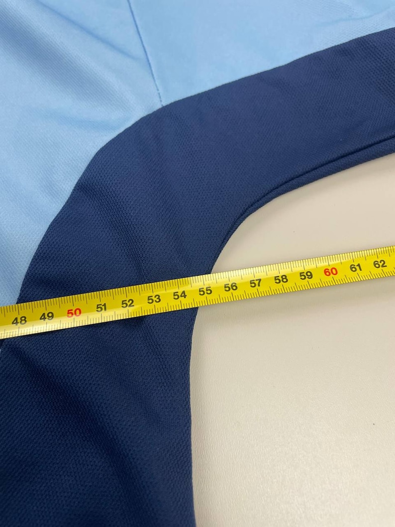May include: A light blue and navy blue garment with a yellow measuring tape laid across it. The tape reads from 48 to 62 inches. The garment appears to be made of a textured fabric.