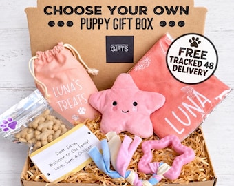 May include: A brown cardboard puppy gift box containing a pink drawstring bag labeled Luna's Treats, a pink star-shaped plush toy, a pink blanket labeled Luna, a bag of bone-shaped treats, a note to Luna, and a pink star-shaped teething ring.