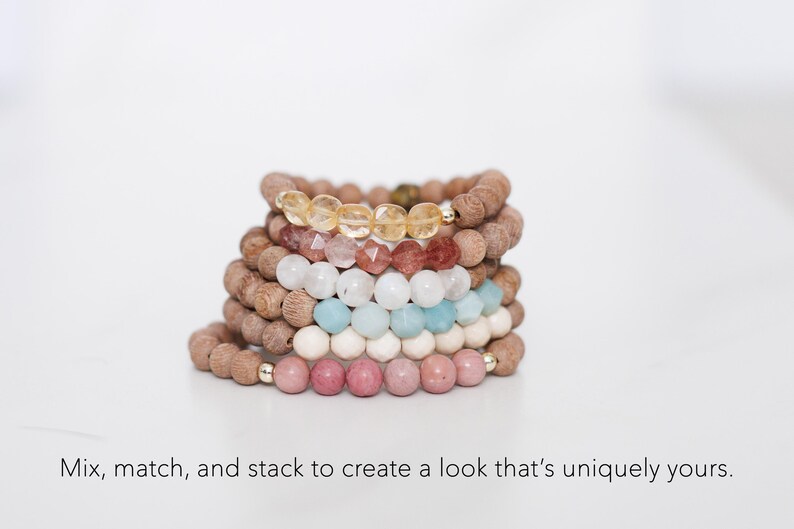 May include: A stack of six beaded bracelets featuring brown wooden beads and faceted gemstone beads in yellow, pink, white, light blue, and cream, with small gold-toned metal accents. The text below reads: Mix, match, and stack to create a look that's uniquely yours.