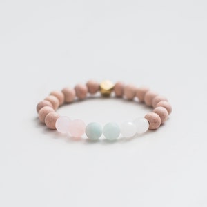 May include: A bracelet made of light brown wooden beads with three gemstone beads: one pink, one light blue, and one white.