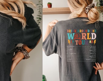 May include: A dark gray t-shirt with a colorful graphic on the front that says "EPCOT WORLD '79 TOUR '82" and a list of cities on the back that says "Drink Around The World '79 TOUR '82".