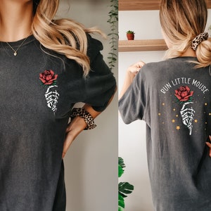 May include: A dark gray oversized t-shirt with a skeleton hand holding a red rose on the front and the text "RUN LITTLE MOUSE" with a skeleton hand holding a red rose and gold stars on the back.
