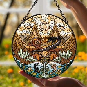 May include: A circular stained glass suncatcher featuring a detailed fantasy landscape with two dragons, two badgers, and two koi fish. The design includes mountain peaks, clouds, crystals, and a central flame, all framed by a black metal chain.