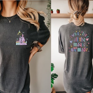 May include: Dark gray t-shirt featuring a colorful castle graphic with Tinkerbell. The back of the shirt displays the text "I long live all the magic we made" in a whimsical font with Mickey Mouse ears and stars.