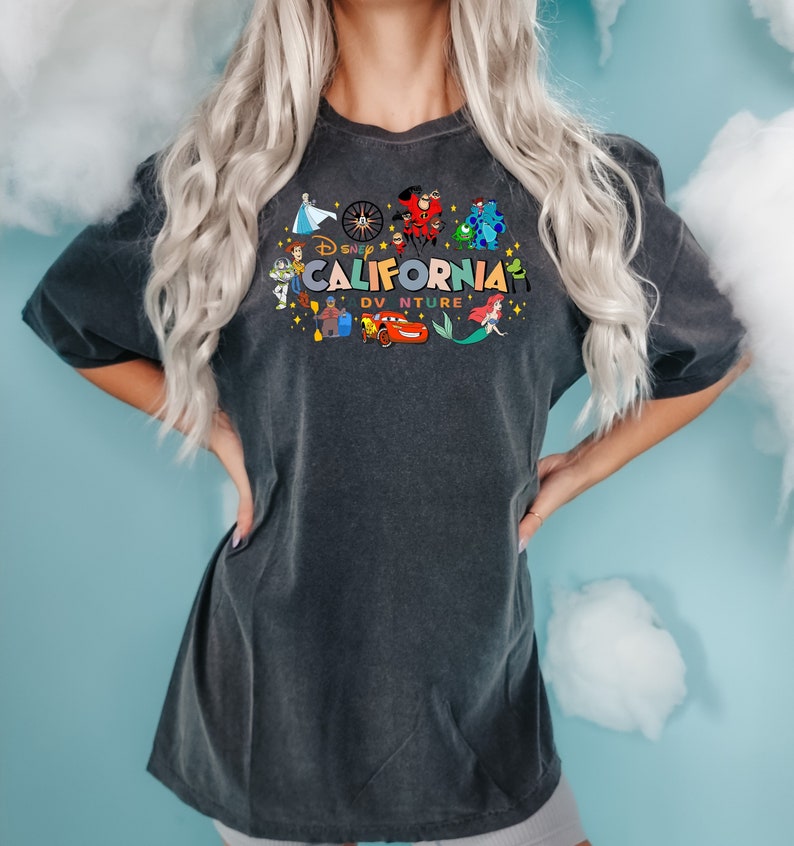 Pu&ograve; includere: Una maglietta nera con una grafica colorata di personaggi Disney e il testo "Disney California Adventure".