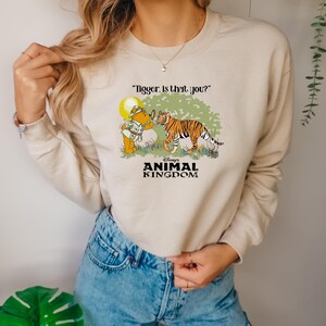 May include: A beige sweatshirt with a graphic of Winnie the Pooh looking through a magnifying glass at Tigger. The text "Tigger. Is that you?" is above the graphic. The text "Disney's Animal Kingdom" is below the graphic.