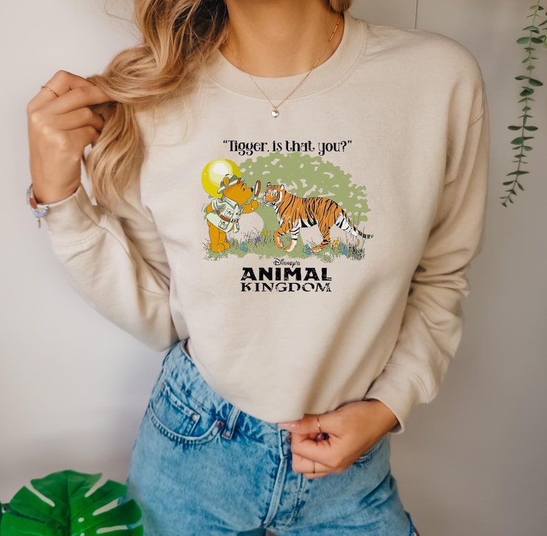 May include: A beige sweatshirt with a graphic of Winnie the Pooh looking through a magnifying glass at Tigger. The text "Tigger. Is that you?" is above the graphic. The text "Disney's Animal Kingdom" is below the graphic.