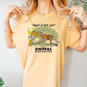May include: A yellow t-shirt with a graphic of Winnie the Pooh looking through a magnifying glass at a tiger. The text "Tigger. Is that you?" is above the graphic. The text "Disney's Animal Kingdom" is below the graphic.