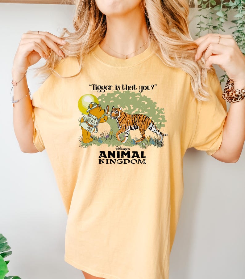 May include: A yellow t-shirt with a graphic of Winnie the Pooh looking through a magnifying glass at a tiger. The text "Tigger. Is that you?" is above the graphic. The text "Disney's Animal Kingdom" is below the graphic.