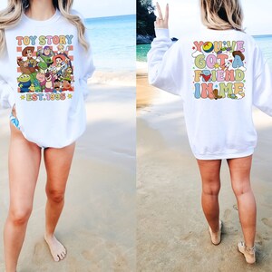 May include: White sweatshirt with a colorful graphic of Toy Story characters on the front and the text "Toy Story Est. 1995" and the text "You've Got a Friend in Me" on the back.