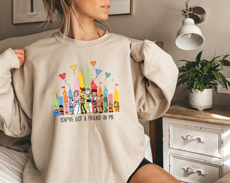 May include: A beige sweatshirt with a colorful graphic of the Disney castle and characters from Toy Story. The text "You've got a friend in me" is printed below the graphic.