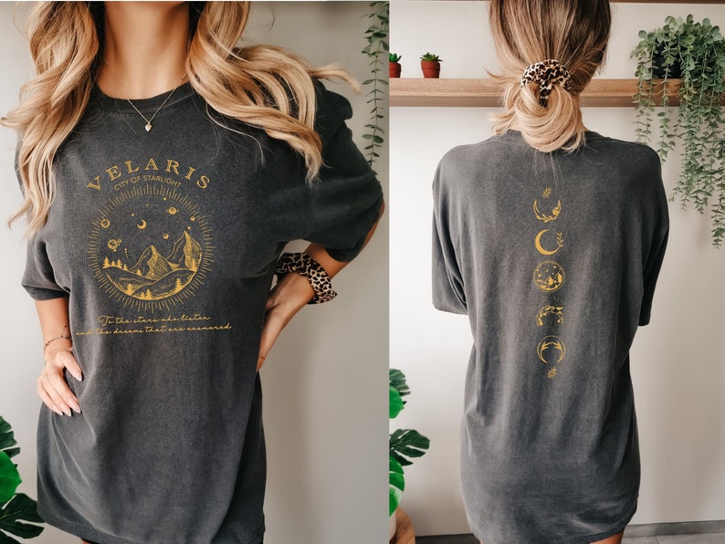 May include: A dark gray oversized t-shirt with a gold graphic on the front that says "Velaris City of Starlight" and "To the stars we listen and the dreams that rise we answer". The back of the shirt has a gold graphic of a crescent moon and stars.