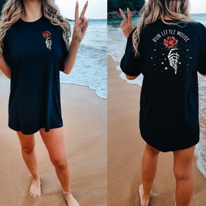 Peut inclure: T-shirt noire surdimensionn&eacute;e avec un motif de main squelettique tenant une rose rouge. Le dos du t-shirt dit "Run Little Mouse" avec un motif de main squelettique tenant une rose rouge et des &eacute;toiles dor&eacute;es.