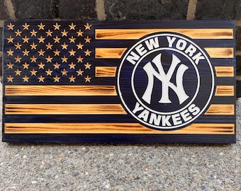 May include: A wooden American flag with a blue and white New York Yankees logo in the center. The flag is distressed and has a rustic look.