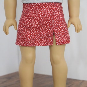 May include: A red skirt with a white floral pattern and a split in the front.