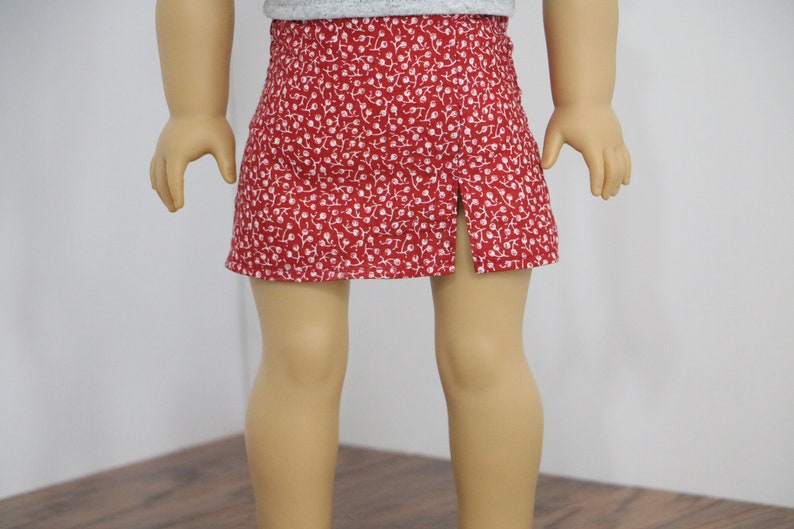 May include: A red skirt with a white floral pattern and a split in the front.