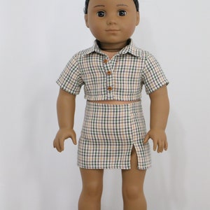 May include: A doll wearing a plaid shirt and skirt set. The shirt is a cropped style with short sleeves and a button closure. The skirt is a mini skirt with a side slit.