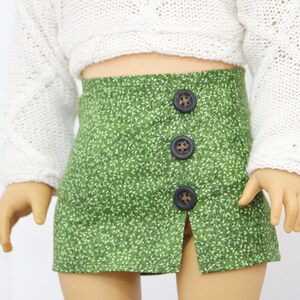May include: A green skirt with a white floral pattern and a front slit. The skirt has three brown buttons down the front.