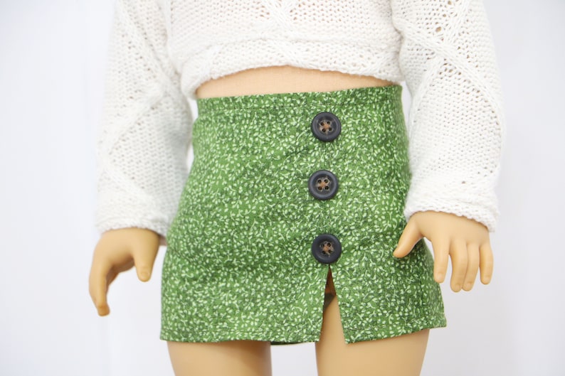 May include: A green skirt with a white floral pattern and a front slit. The skirt has three brown buttons down the front.