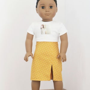 May include: A doll wearing a white t-shirt with a photo printed on the front and a yellow skirt with white polka dots.